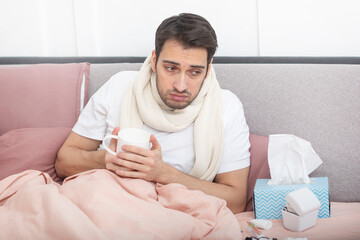 Sick man lying in the bed, suffering from high fever and flu. He tries to treat himself at home