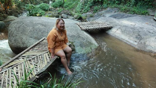 Asian fat woman Tourist stiing on bamboo bridge handmade at vacation holiday natural waterfall. Tourism travel and vacation concept