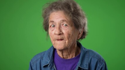 Closeup slow motion portrait of toothless elderly senior old woman with wrinkled skin and grey hair put hand to mouth to tell a secret, a isolated on green screen background studio