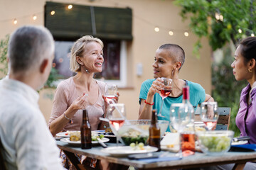 Female friends enjoying conversation together at summer dinner at home - Women having fun drinking and eating