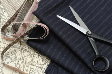 Tailoring. Tailor's scissors are lying on a piece of blue fabric. A paper pattern and a tailor's centimeter are lying on the desktop next to it.