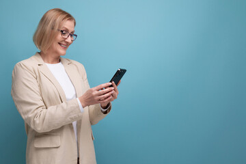 Fototapeta premium a middle-aged woman with a bob haircut in a classic jacket pays for a purchase on the Internet using a credit card on a bright background with copy space