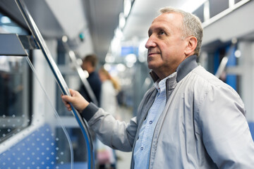 Mature man standing in subway and holding handrail