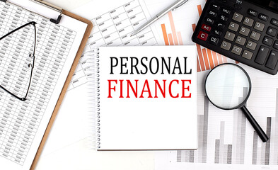 PERSONAL FINANCE text on notebook with clipboard and calculator on a chart background