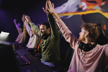 Cheerful indian player giving high five to friends near computers in cyber club.