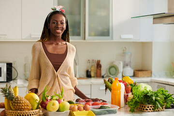 Portrait of smiling young Black woman standing at kitchen counter with fresh groceries