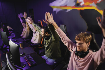 Smiling indian man giving high five to friends near computers in gaming club.