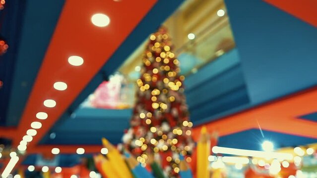 Huge Christmas tree decorated with red bows and balls, plush toys, shining lights. Impressive traditional holiday decorations with red boxes and gifts in a trade center. Winter feast in a toy store. 