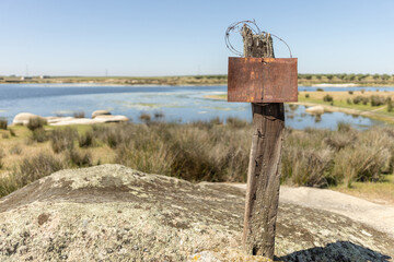 wooden post with an empty sign, on top to write a message, in the background you can see a lake out of focus