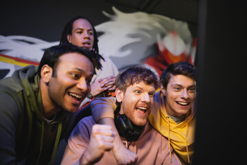 Obraz premium Excited multiethnic gamers looking at computer monitor in gaming club.