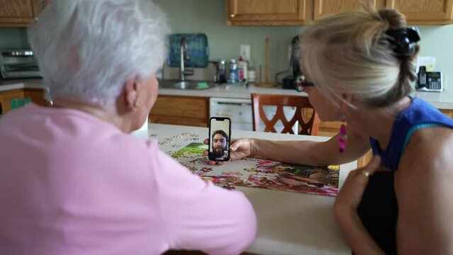 Happy smiling, happy elderly senior woman with mature middle aged daughter having video chat on phone with son. Smiling blonde talking to family on smartphone.