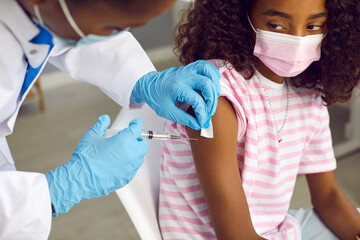 Woman doctor or pediatric nurse giving intramuscular arm injection to child. Afro American school...