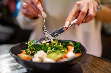 Woman's hands eat greek salad on table in restaurant