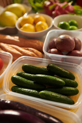 Plastic container with fresh cucumbers on kitchen table nest to other groceries