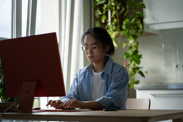 Concentrated pensive Asian woman student typing essay for grant application wishes to get free education. Attentive focused Chinese girl freelancer sits at desk working with computer in home office