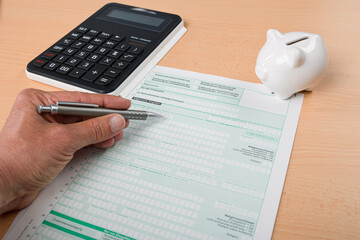 Close Up of filling out a tax declaration with a calculator, a hand with a pen and a piggy bank