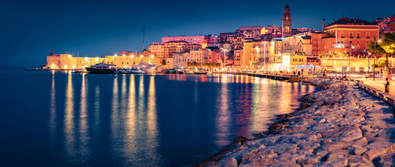 Fototapeta premium Illuminated quay in Gaeta town with Cathedral Basilica of Gaeta church on background. Panoramic evening view of coast of Mediterranean sea, Italy, Europe. Traveling concept background.