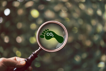 Carbon footprint with magnifying glass on green background. Carbon Footprint is total amount of...