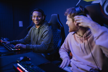 Smiling indian gamer in headphones sitting near blurred friend in cyber club. © LIGHTFIELD STUDIOS