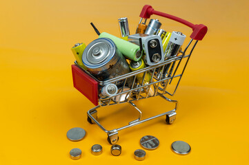 Supermarket trolley with batteries and accumulators of different sizes. Bright yellow background.