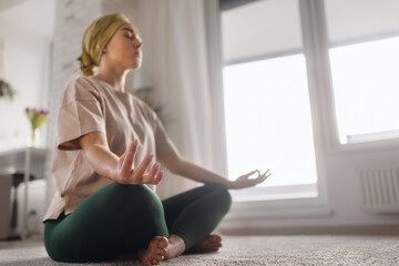 Young woman with cancer taking yoga and meditating in her apartment.