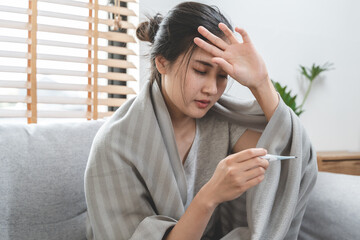 Sick day at home in winter season. Young asian woman have a fever checking thermometer and measure body temperature.