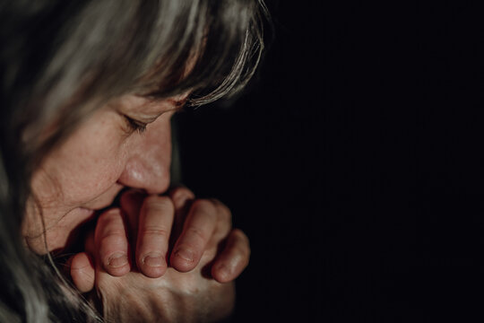 Close-up of unhappy elderly woman praying, black background.