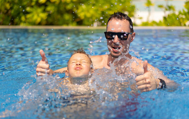 Father and son have fun in the pool in Maldives and show thumbs up