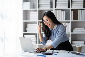 Overjoyed Asian businesswoman in glasses celebrating success withe her laptop computer.