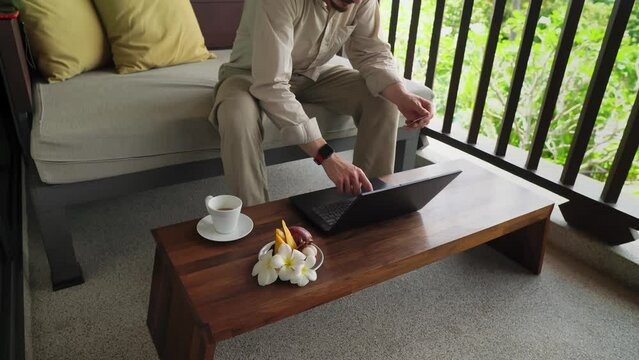 Man is buying things in the internet typing credit card number in laptop sitting on balcony. Male caucasian person is doing online shopping. He inputs pincode in computer. Spending money in cyberspace