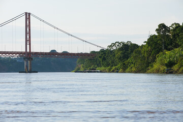 Puerto Maldonado Billinghurst red bridge with Amazon river, blue sky, forest background in Peru. Selective focus of river. Open space area. 