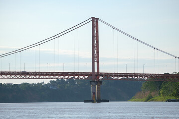 Puerto Maldonado Billinghurst red bridge with Amazon river, blue sky, forest background in Peru. Selective focus of river. Open space area. 