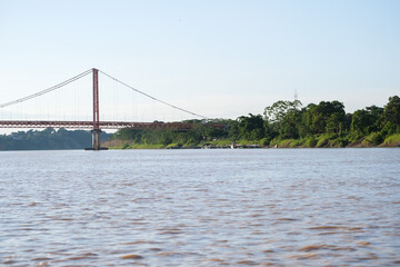 Fototapeta premium Puerto Maldonado Billinghurst red bridge with Amazon river, blue sky, forest background in Peru. Selective focus of river. Open space area. 