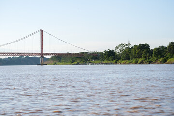 Puerto Maldonado Billinghurst red bridge with Amazon river, blue sky, forest background in Peru. Selective focus of river. Open space area. 