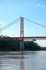 Puerto Maldonado Billinghurst red bridge with surface reflection on Amazon river, blue sky, forest background in Peru. Selective focus of river. Open space area. 
