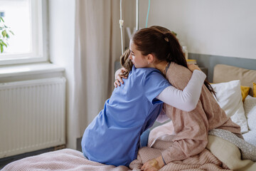 Young doctor hugging teenage girl in hospital room.