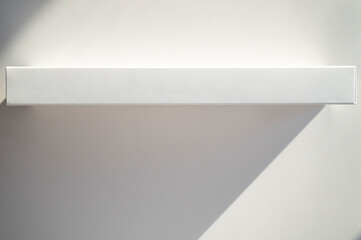 Long thin cardboard white box on paper surface with shadows and sunlight as mockup, top view, space...