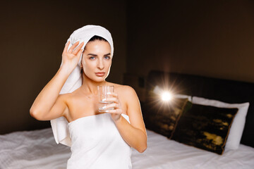 Young serene relaxed woman with bath towel drinking water after taking shower bath at home. Beauty treatment, hydration concept.