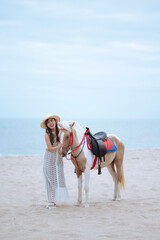 Young long hair woman in white dress riding horse on seascape background