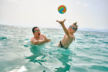 Happy family outdoors summer, father and son bonding, play ball, swim in the sea looking at view enjoying summer vacation. Togetherness Friendly holiday concept.

