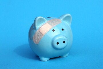 On a blue background there is a piggy bank with a sealed plaster.	