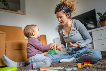 One young woman a mother playing at home on the floor with her one year old child, family playtime,...