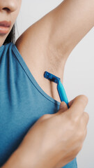 Use a razor, Young confident asian chinese female armpit with blue tank top isolated background.