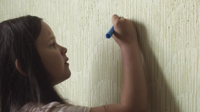 Little girl diligently draw animal with blue marker on wallpaper side view closeup, practice artistic skills. Space for painting, disorderly conduct, drawing, paperhanging damage, childish fantasy.
