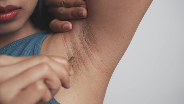 Use tweezers to pull armpit hairs. Young confident asian chinese female armpit with blue tank top isolated background.