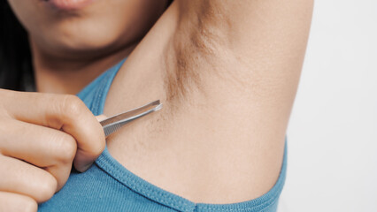 Obraz premium Use tweezers to pull armpit hairs. Young confident asian chinese female armpit with blue tank top isolated background.