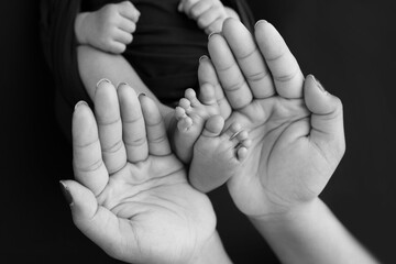 Black and white shade beautiful shape hands of mother, hold tiny newborn baby feet on black background with love, care, family safety and protection, child with premature birth concept or NICU care