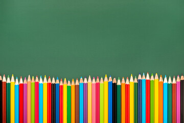 multicolored pencils is on green chalkboard background, top view, copy space, back to school concept