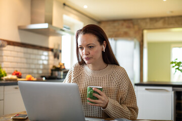 Young woman working on her laptop in the kitchen