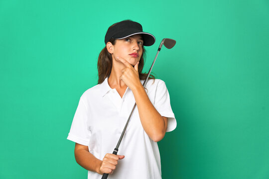 Young caucasian golfer holding a golf stick isolated Young caucasian gollooking sideways with doubtful and skeptical expression.